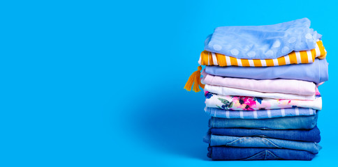 Stack folded colorful clothing summer, jeans on blue background