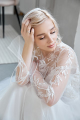 Obraz na płótnie Canvas Ideal bride sitting on the floor, portrait of a girl in a long white dress. Beautiful hair and clean, soft skin. Wedding hairstyle blonde