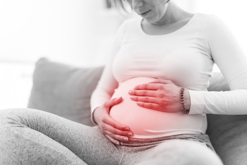 Pregnant tired exhausted woman with stomach issues at home on a couch, being sick.