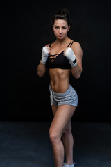 Muscular young woman athlete standing on black background