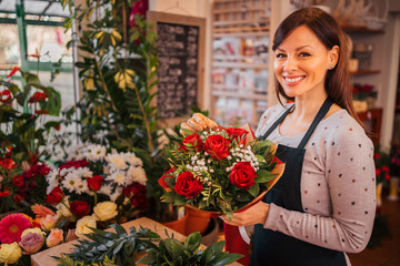 Portrait of a beautiful florist in apron holding rose bouquet. - obrazy, fototapety, plakaty