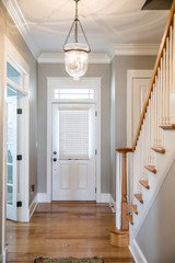 View of a white front door entrance in a new construction house with a hanging chandelier clear glass light and a staircase