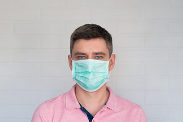 Portrait of dark hair european man in surgery face mask in pink polo on white bricks background