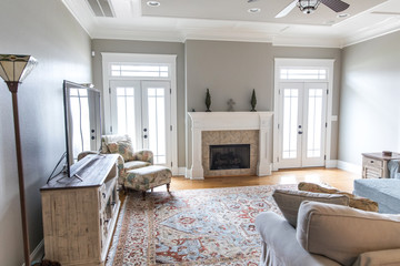 a bright and airy neutral beige living room den in a new construction house with a white and tiled fireplace as the main focal point as well as a decorative rug and lots of natural window light.