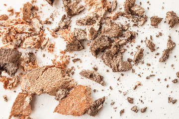 Eyeshadows of neutral beige and brown shades are scattered on a light surface. Detailed macro photo. The concept of decorative cosmetics.