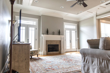 a bright and airy neutral beige living room den in a new construction house with a white and tiled fireplace as the main focal point as well as a decorative rug and lots of natural window light.