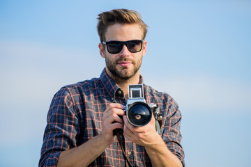 Blogger shooting vlog. Handsome blogger guy traveler retro camera. Manual settings. Photojournalist concept. Travel blogger. Guy outdoors blue sky background. Vintage equipment. Reporter taking photo