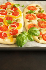 Fototapeta na wymiar Il concetto di cibo italiano. Focaccia non cotta fatta in casa con verdure e foglie di basilico su una teglia. Avvicinamento.