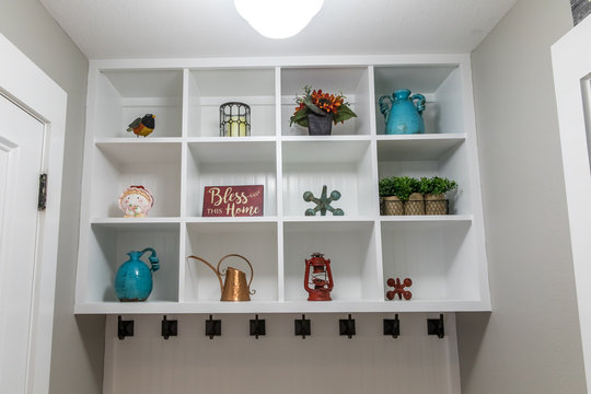 Hallway mud room in a new construction house home with white wooden shelves with decorative items, hooks for hanging jackets