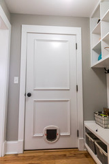 A white door to the garage with a pet cat dog small door and hardwood floors in a new construction home house