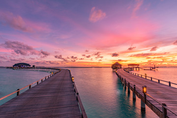 Naklejka na ściany i meble Amazing sunset landscape. Picturesque summer sunset in Maldives. Luxury resort villas seascape with soft led lights under colorful sky. Dream sunset over tropical sea, fantastic nature scenery