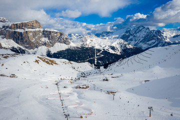 Fototapeta na wymiar Landscape at a ski resort Campitello di Fassa Italy. Winter Dolomites and blue sky with clouds. Aerial view on ski slopes and ski lifts