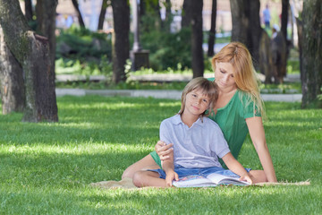 Fototapeta premium Family reading. Mom and son are reading book on grass