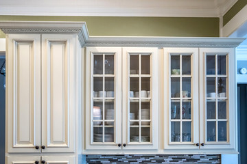 Glass door cabinets in a a square shaped green kitchen with cream colored cabinets in a new construction home with granite countertops and lots of cabinets and storage space