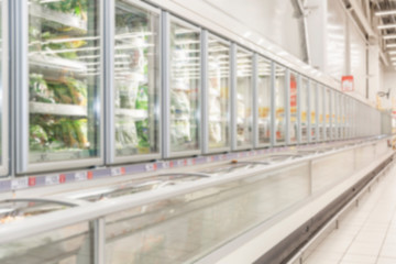 Rows of frozen food display cases in a large supermarket. Blurred.
