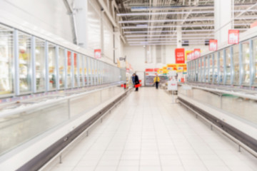 Naklejka premium Rows of frozen food display cases in a large supermarket. Blurred.