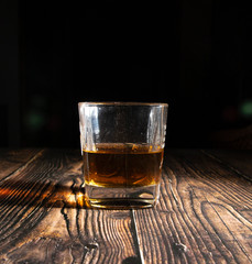 Whiskey with ice cubes on a wooden table. An old tabletop with light and a glass of strong drink.