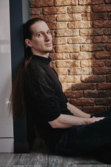 a man in a black turtleneck against a brick wall. light a thin beam from the window.