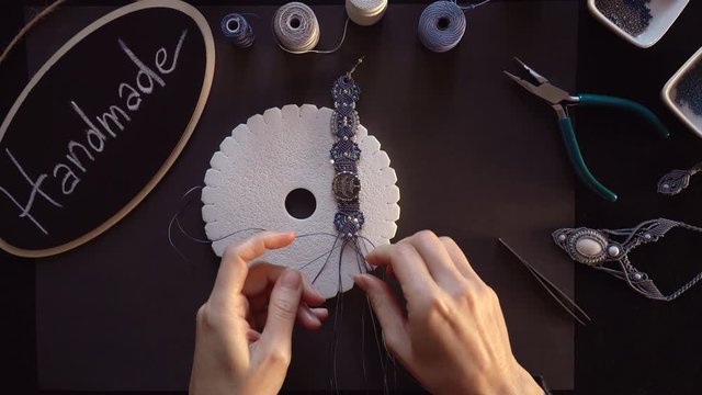 Lifestyle concept, reinvent your life and your job: flat lay top view of macrame jewels with colored spools of thread, a bracelet, beads, tools and a little blackboard with text handmade chalked