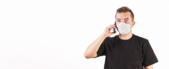 Young man wearing home made cotton face mouth nose virus mask talking on his mobile phone. White background, wide banner  space for text - can be used during coronavirus covid-19 outbreak