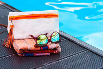 beach sun glasses, cosmetic bag,  cover-up beachwear wrap near swimming pool, tropical background.