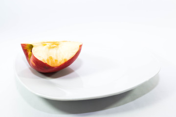 Half red apple with a missing bite on a white plate on white background.