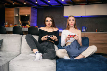 Obraz premium Two girlfriends passionate playing computer games at home while having quarantine. World pandemic home isolation. Enjoying time to spend leisure.