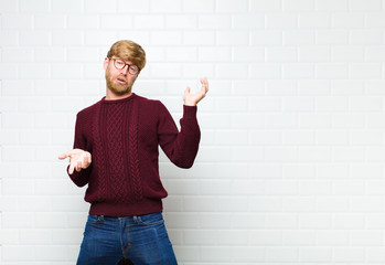 young blonde man shrugging with a dumb, crazy, confused, puzzled expression, feeling annoyed and...