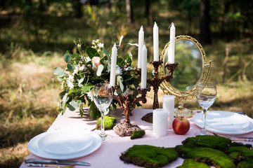 the table is decorated with flower and tableware decor, henchmen, plates and moss