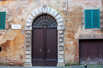 old massive iron doors in a medieval house with dilapidated plaster on the wall, Piazza del Conte, Siena, Italy