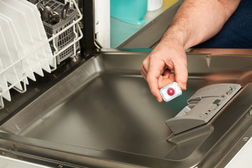 Mano de hombre poniendo una tableta en caja de detergente en un lavavajillas. Vista superior