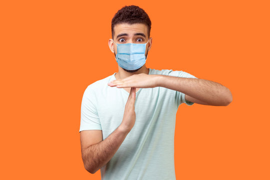 I Need More Time! Portrait Of Frustrated Brunette Man With Surgical Medical Mask Showing Time Out Gesture, Looking With Imploring Eyes, Hurry To Meet Deadline. Studio Shot On Orange Background