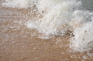 White foam and splashes of the sea running onto a sandy beach