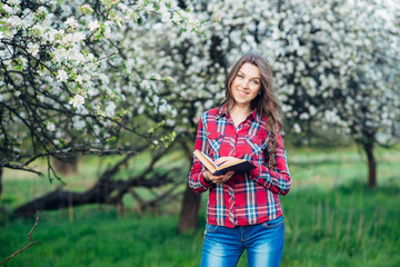 Young woman in with book in a blooming garden