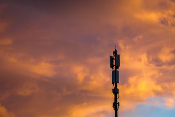 Cellular communications tower on vivid dramatic clouds background in evening, copy space.