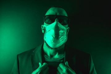 A young Caucasian man with a scarf and sunglasses in the coronavirus pandemic with a green background, Covid-19