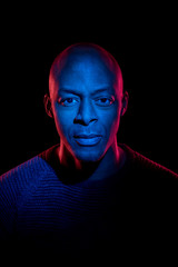 Black man with blue and red light looking at the camera, isolated on black background....