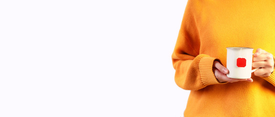 Woman in orange cozy sweater holding red cup of hot drink on white background. Copyspace, close up, banner