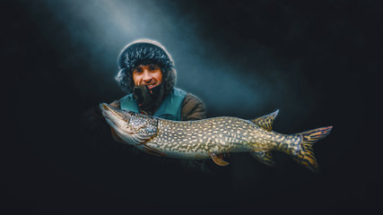 Happy angler holds a trophy pike in his hands.