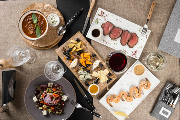 dinner table with shrimp, roast beef, salad, cheese platter and wine served at home or at restaurant