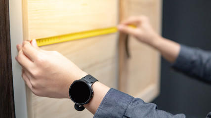 Male hand using tape measure on cabinet panel choosing materials or countertops for built-in furniture design. Shopping furniture and house decoration. Home improvement concept