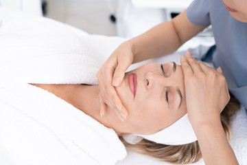 Fototapeta na wymiar Close-up of aesthetic professional sculpting face of mature woman with massage, relaxed woman enjoying beauty treatment procedure