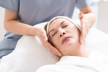 Fototapeta na wymiar Close-up of beautician massaging face of mature female client relaxing at procedure