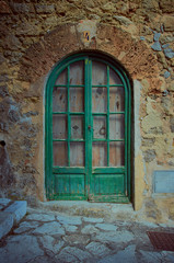Fototapeta na wymiar Wooden front door in a facade of an ancient house. The facade is made of stones and the street as well. It is summer in Mallorca, Spain.