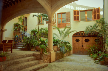 Inner courtyard with lot of plants. There is a porch with a wooden table and chairs. There are two wooden windows, a wooden door and stairs to go to the main door. Mallorca, Spain 08/17