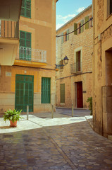 Pedestrian street in a small town. The street is made of stones and the houses too. Green doors and windows. It is summer in Mallorca, Spain.