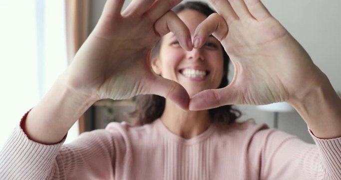 Smiling young woman volunteer showing hands sign heart shape looking at camera. Healthy heart health life insurance, love and charity, voluntary social work, organ donation concept, close up portrait.