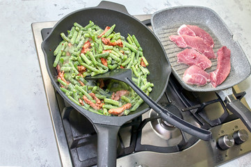  healthy kitchen, fried green beans, in a pan on a stove on a marble countertop and sliced pork in a pan next to