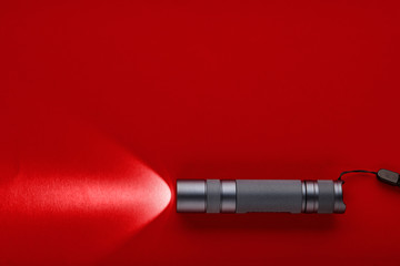 Flashlight on a red background. A beam of light from a flashlight. Finning on the metal body.