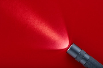 Flashlight on a red background. A beam of light from a flashlight. Finning on the metal body.